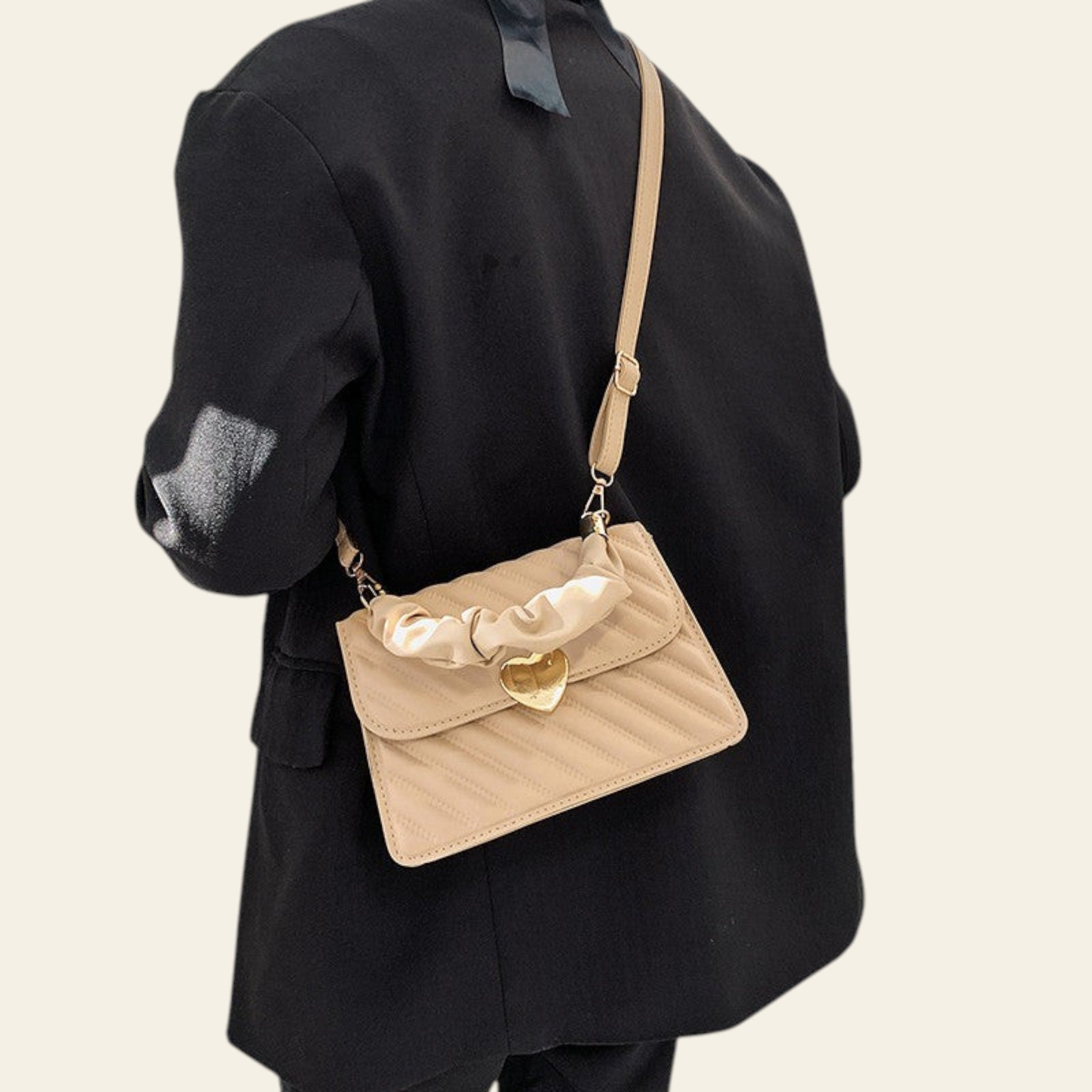 Person wearing a black outfit with a beige quilted handbag featuring a heart-shaped clasp.