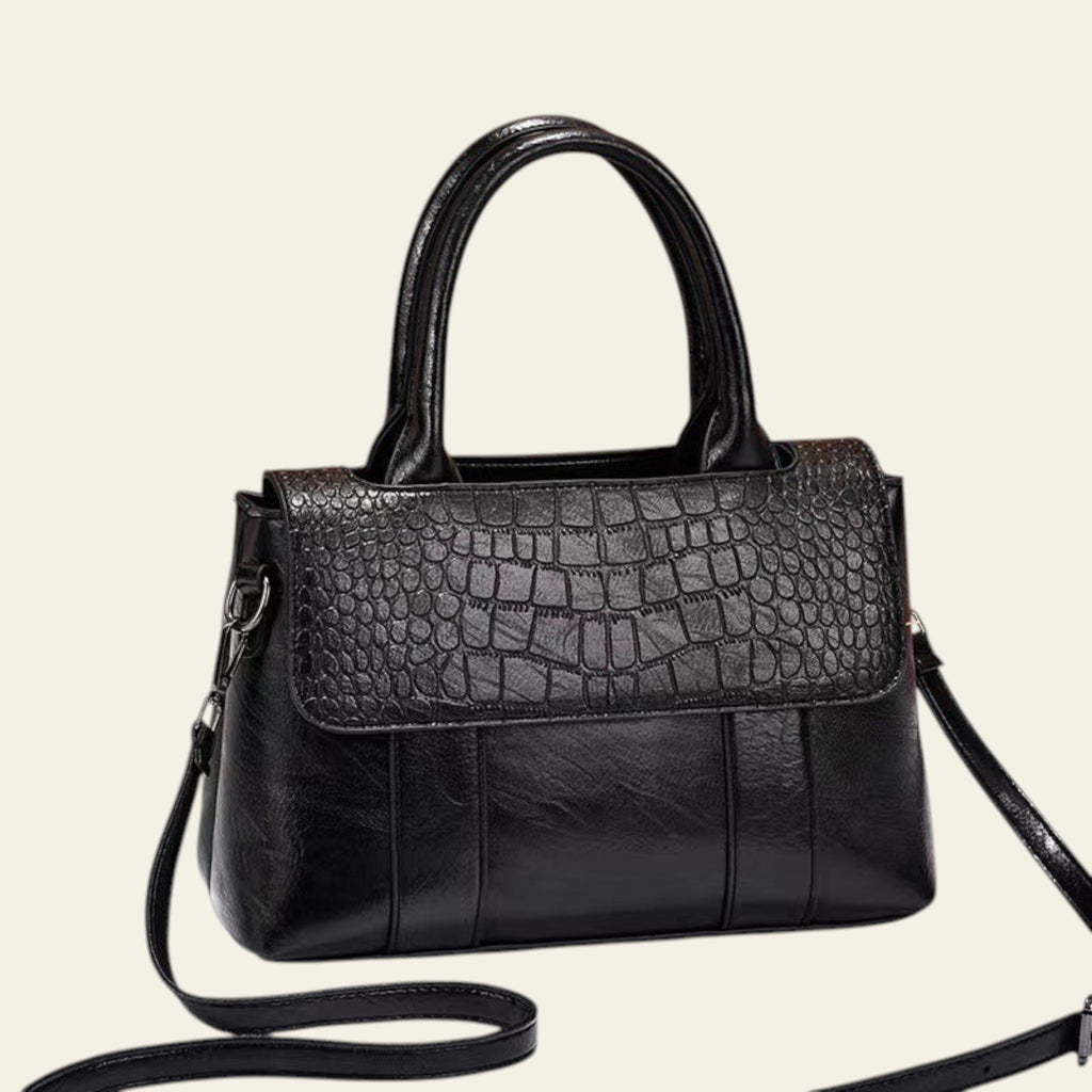 Black handbag with crocodile texture on a white surface with a brown background