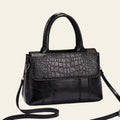 Black handbag with crocodile texture on a white surface with a brown background