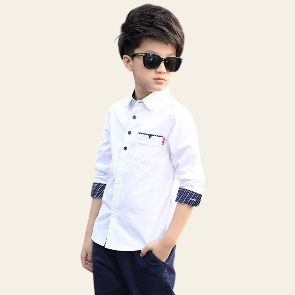 Child wearing a white shirt with a small logo and dark pants, standing on a street.
