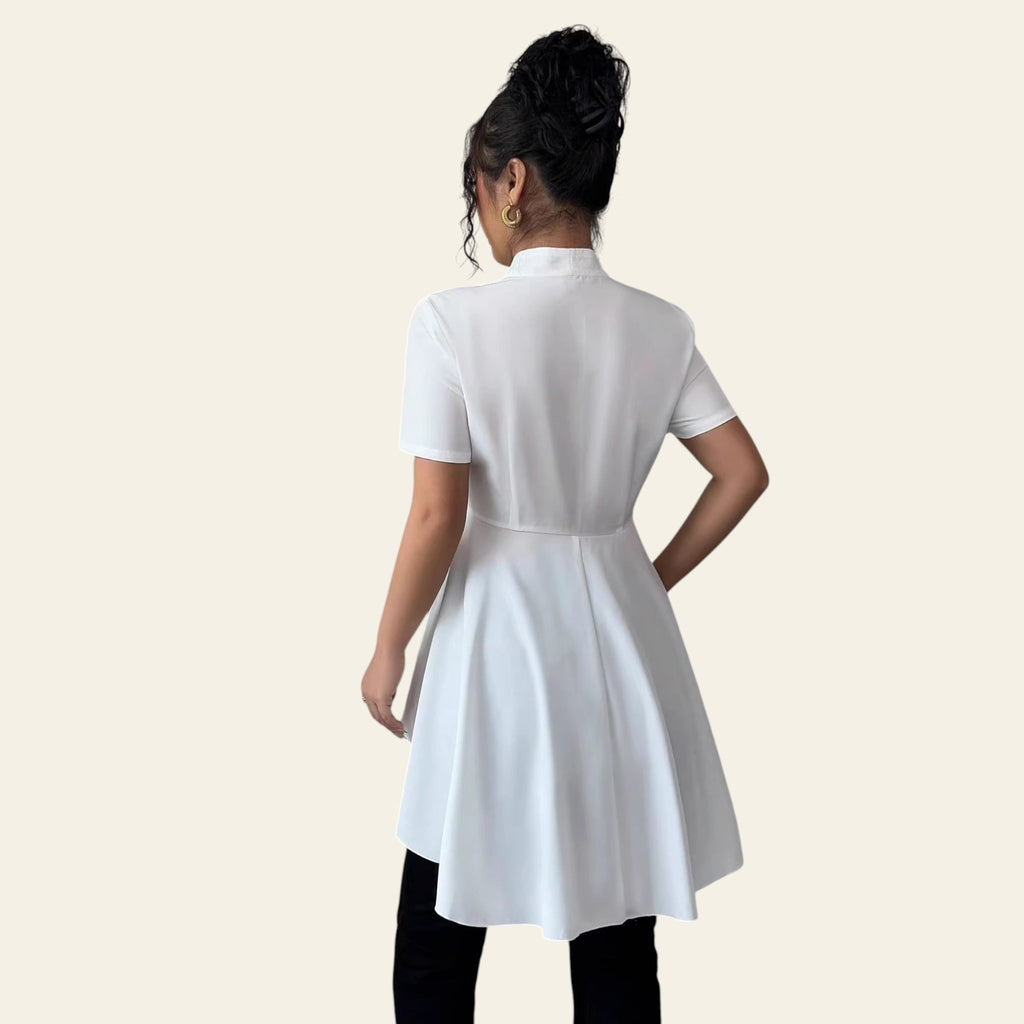 Person wearing a white dress standing in a room with light gray walls and white curtains.
