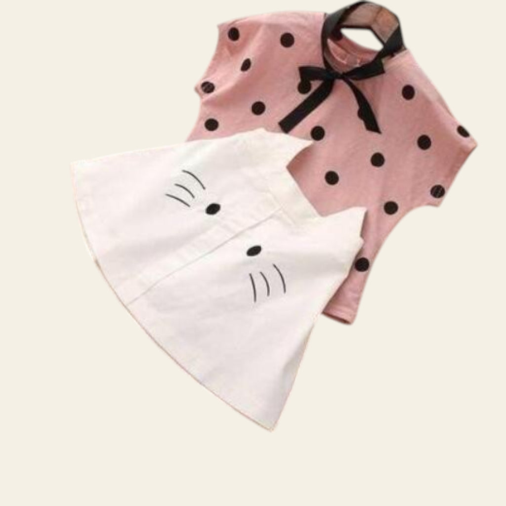 Pink polka dot dress with black bow and white cat-shaped towel on a wooden surface