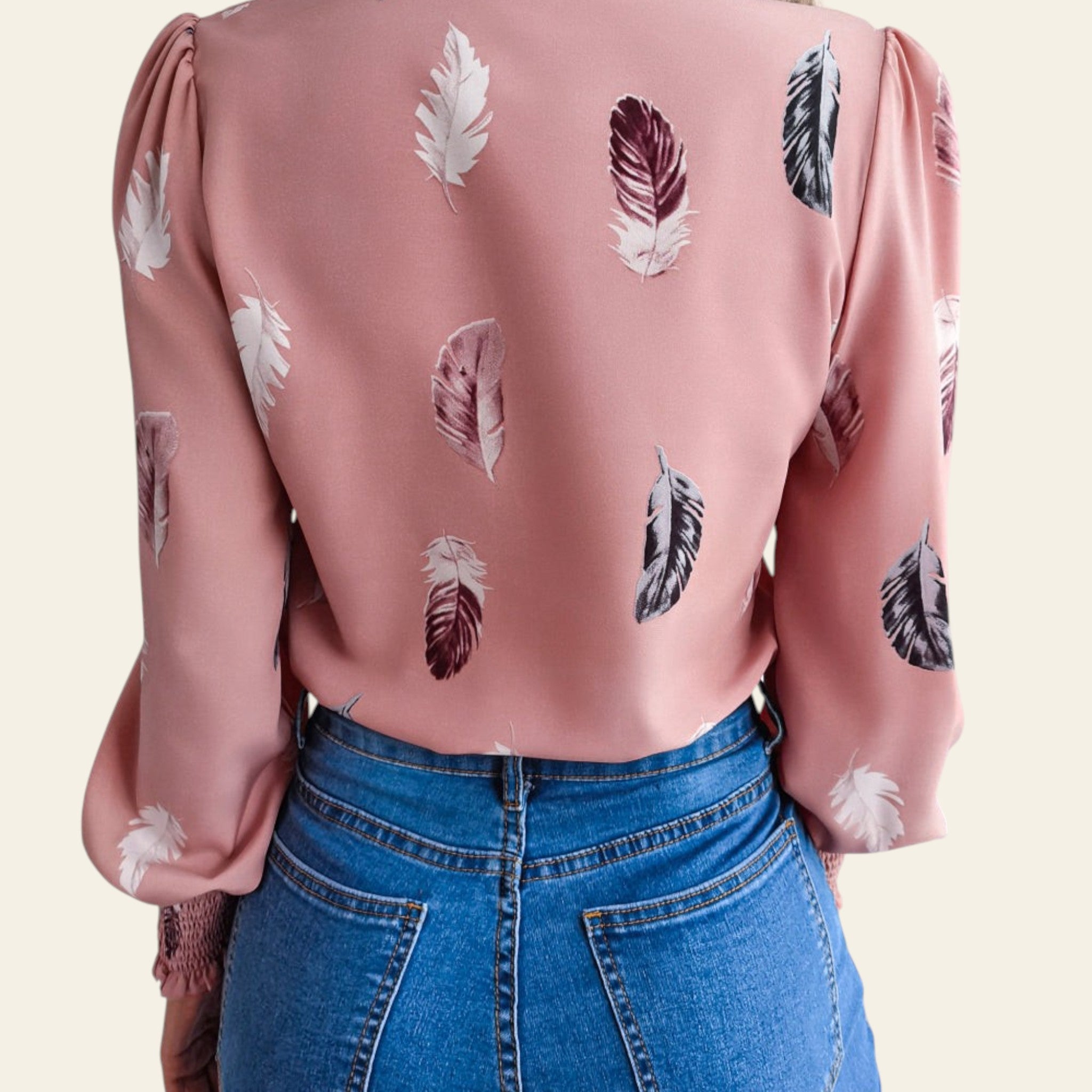 Person wearing a pink blouse with feather pattern and blue jeans on a neutral background