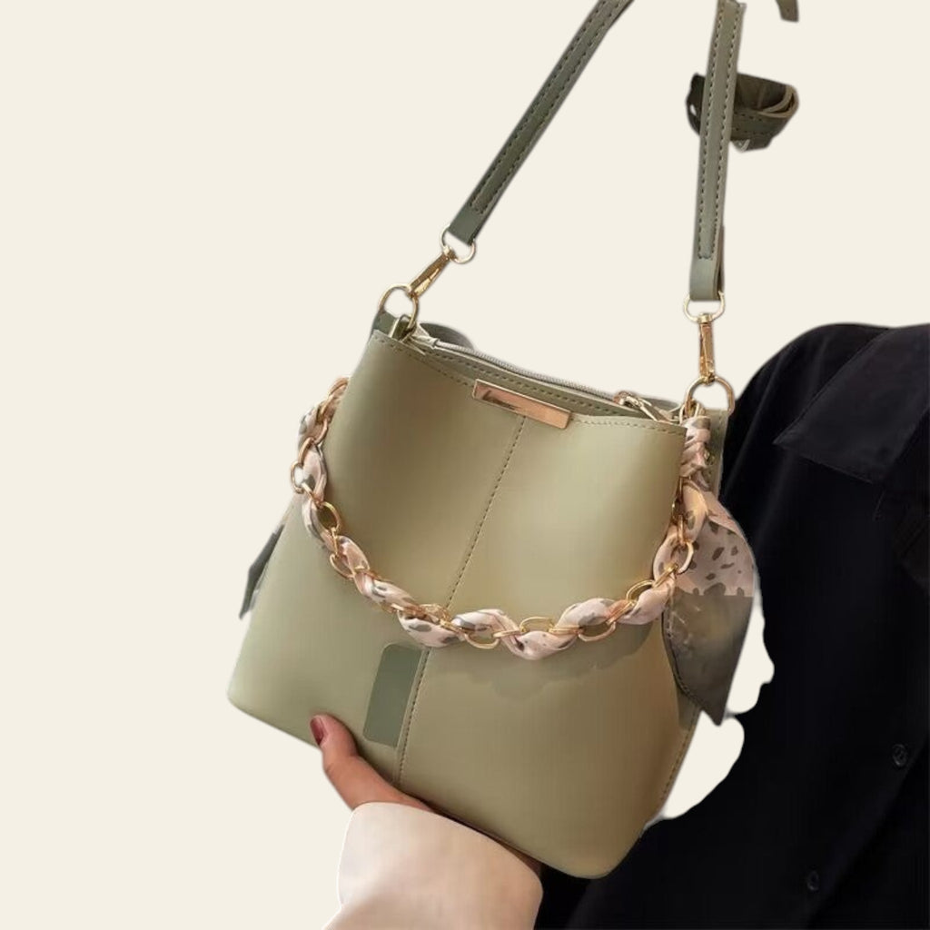 Light green handbag with a decorative chain strap held by a person against a neutral background