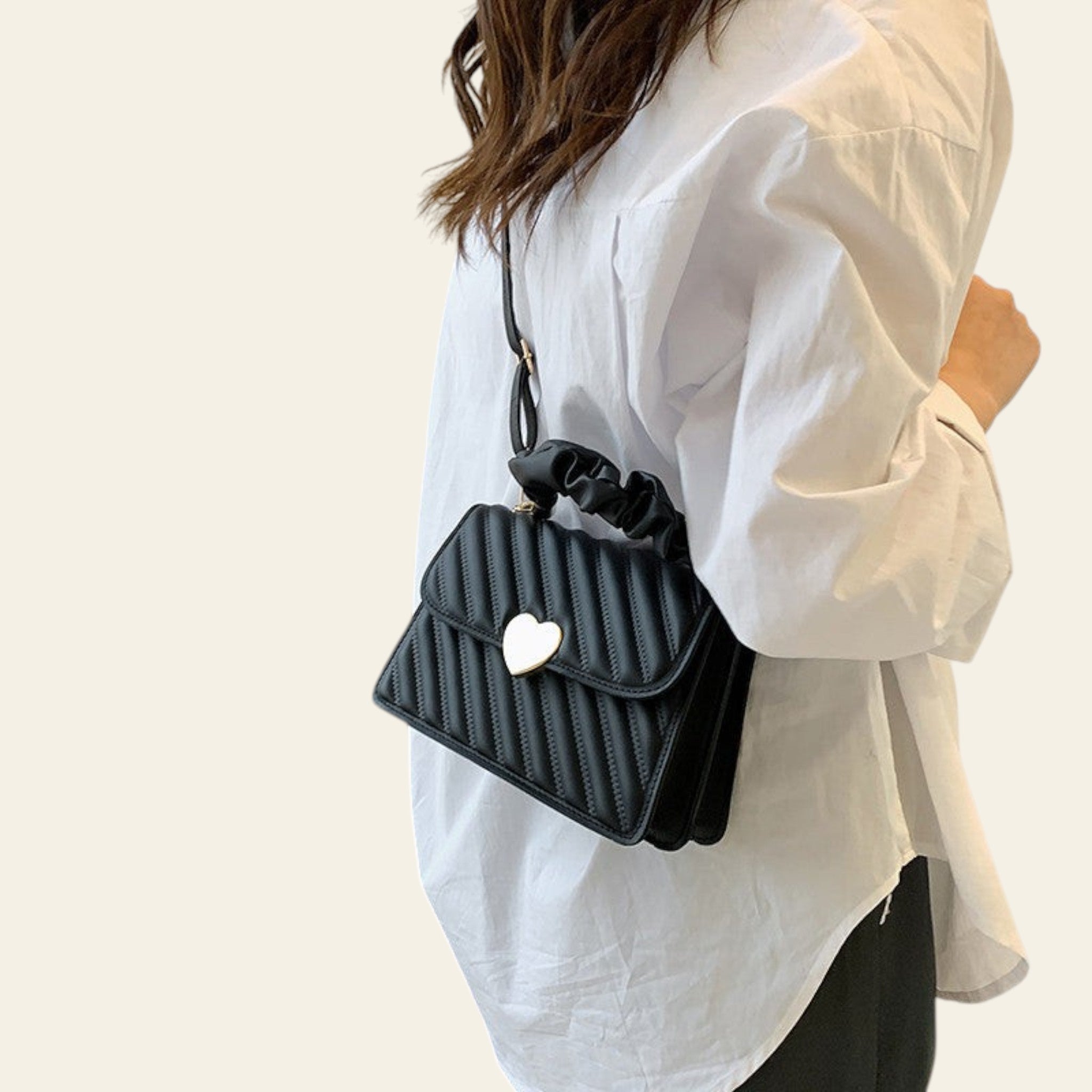 Person holding a black handbag with a heart detail in a room setting.