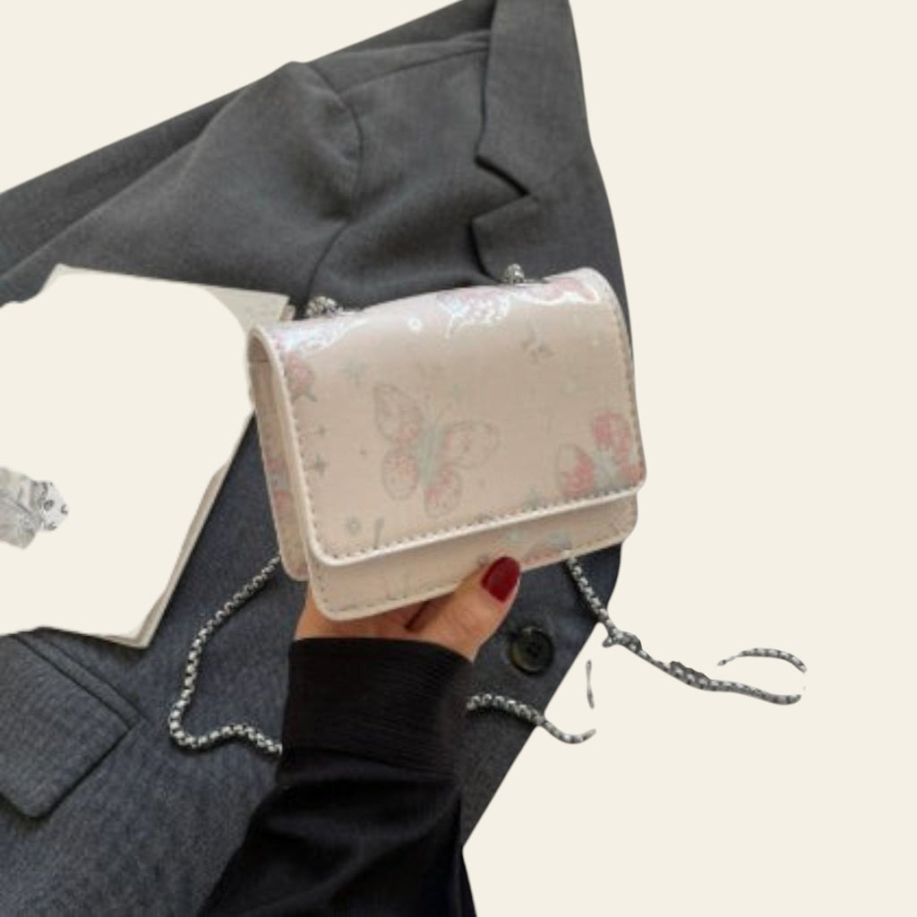 Hand holding a small pink handbag with floral design on a white surface