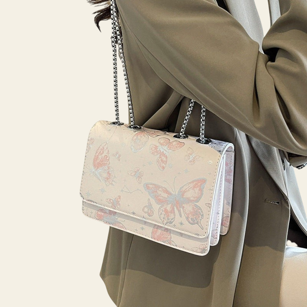Handbag with butterfly design held by a person wearing a beige coat.