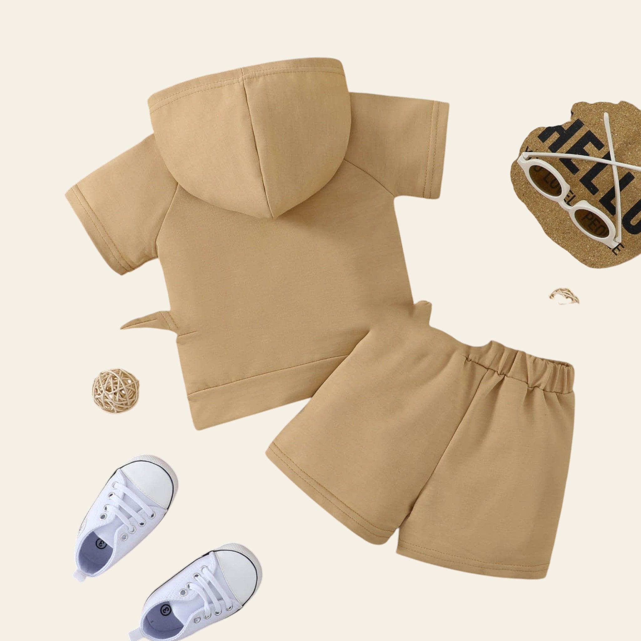 Beige hoodie and pants set on a wooden surface with white sneakers and sunglasses.