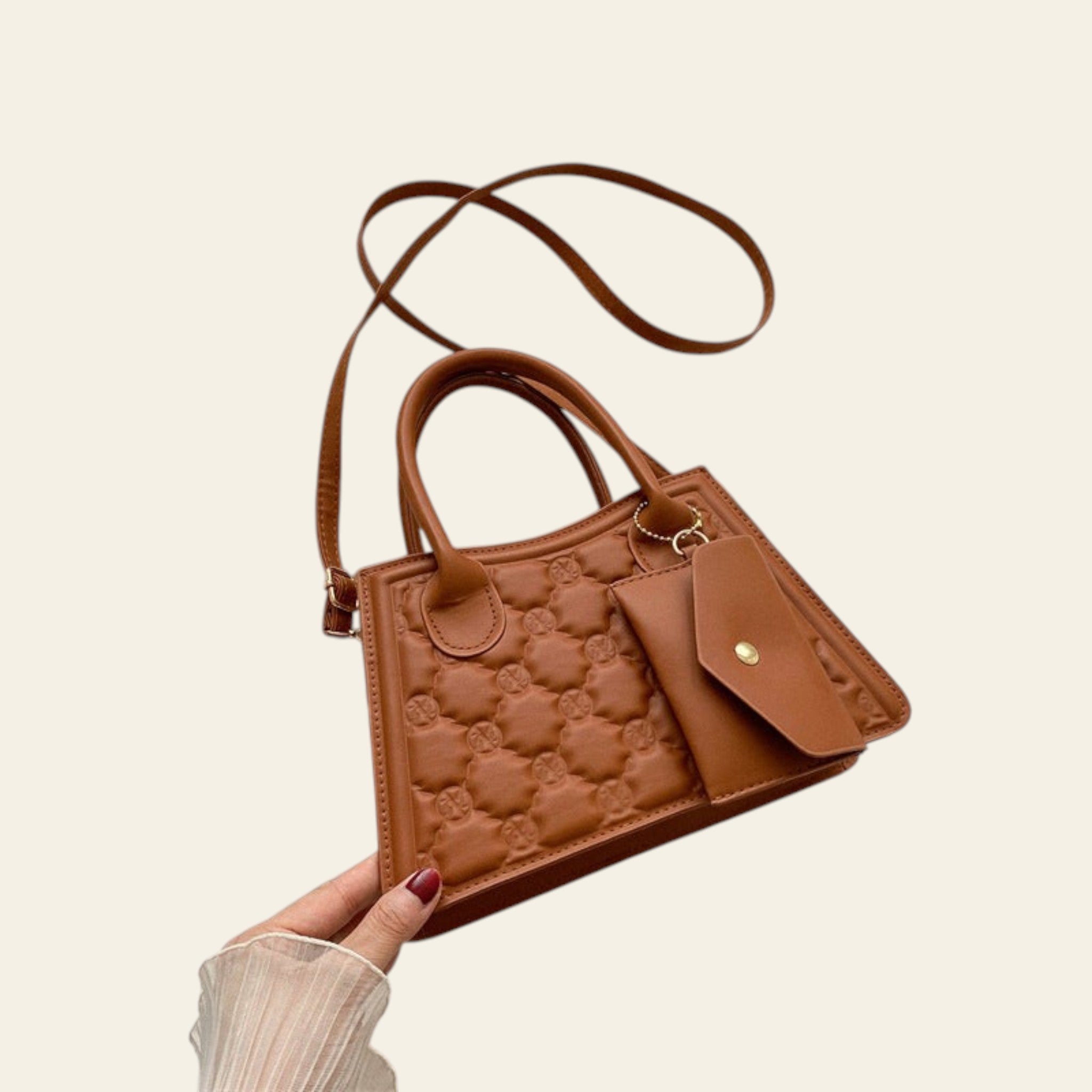 Brown quilted handbag held by a hand on a light background