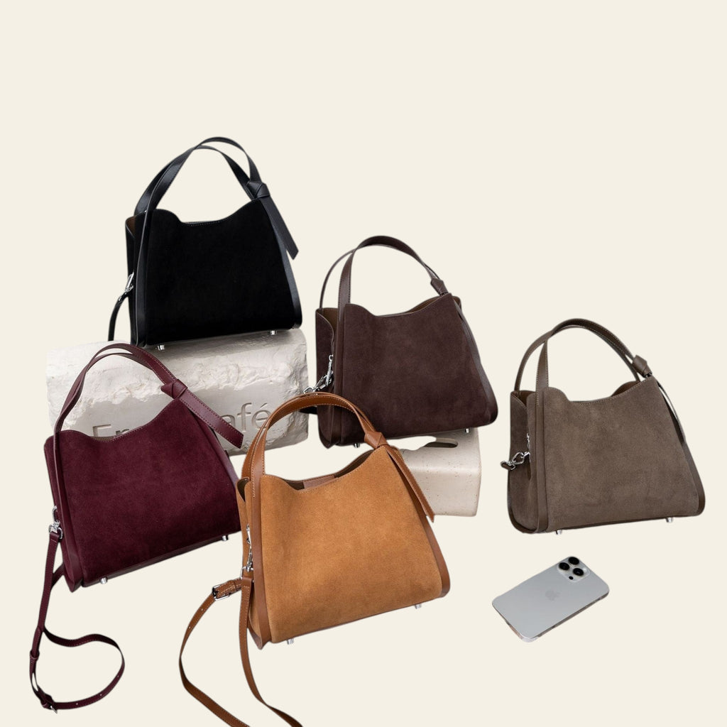 Five handbags in various colors on a bench with a light gray wall background.