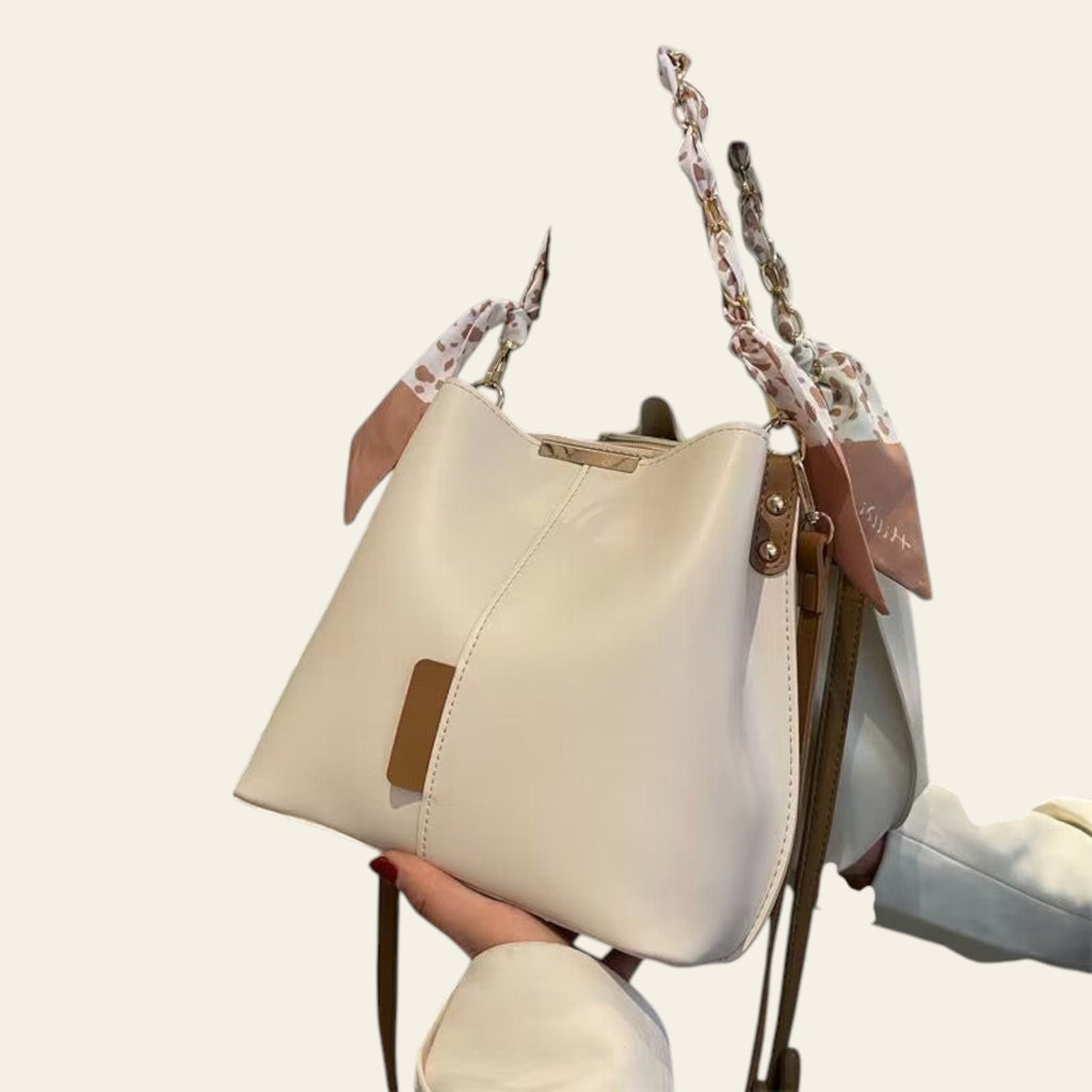 White handbag with floral chain strap held by a person against a neutral background