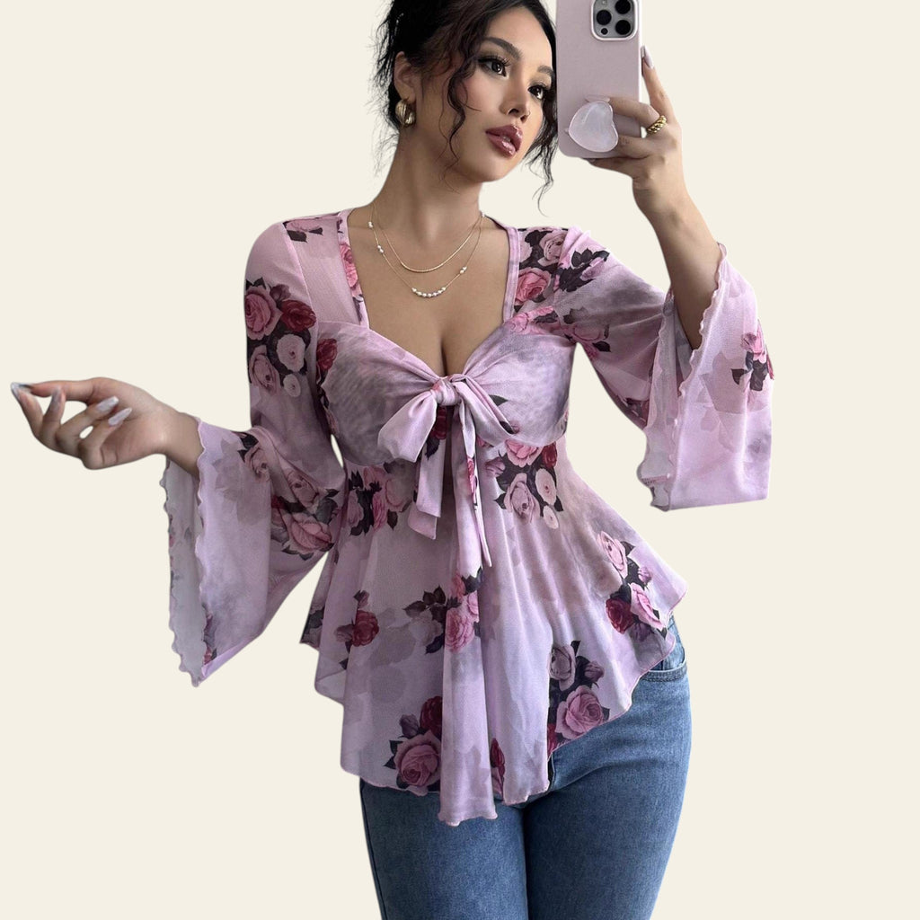 Woman wearing a pink floral blouse with bell sleeves taking a mirror selfie.