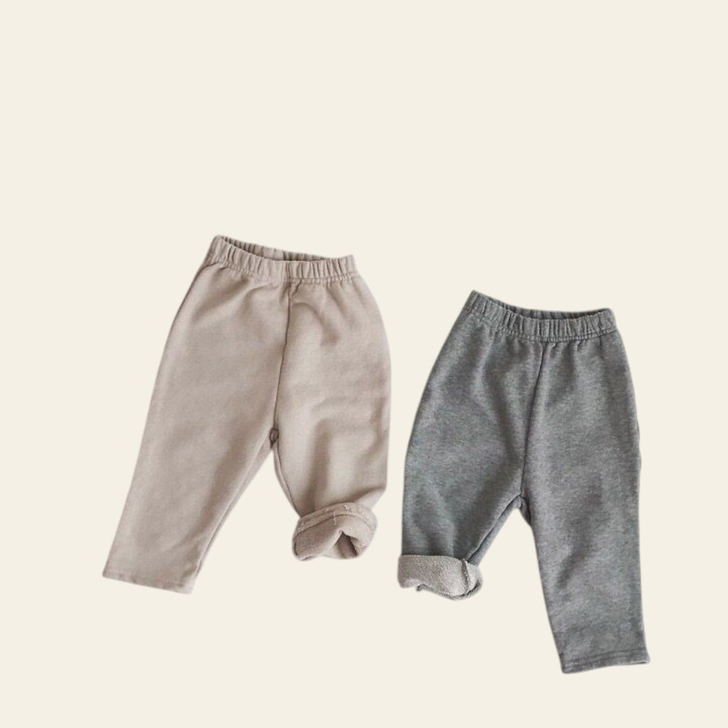 Two pairs of baby pants, one beige and one gray, on a light gray background.