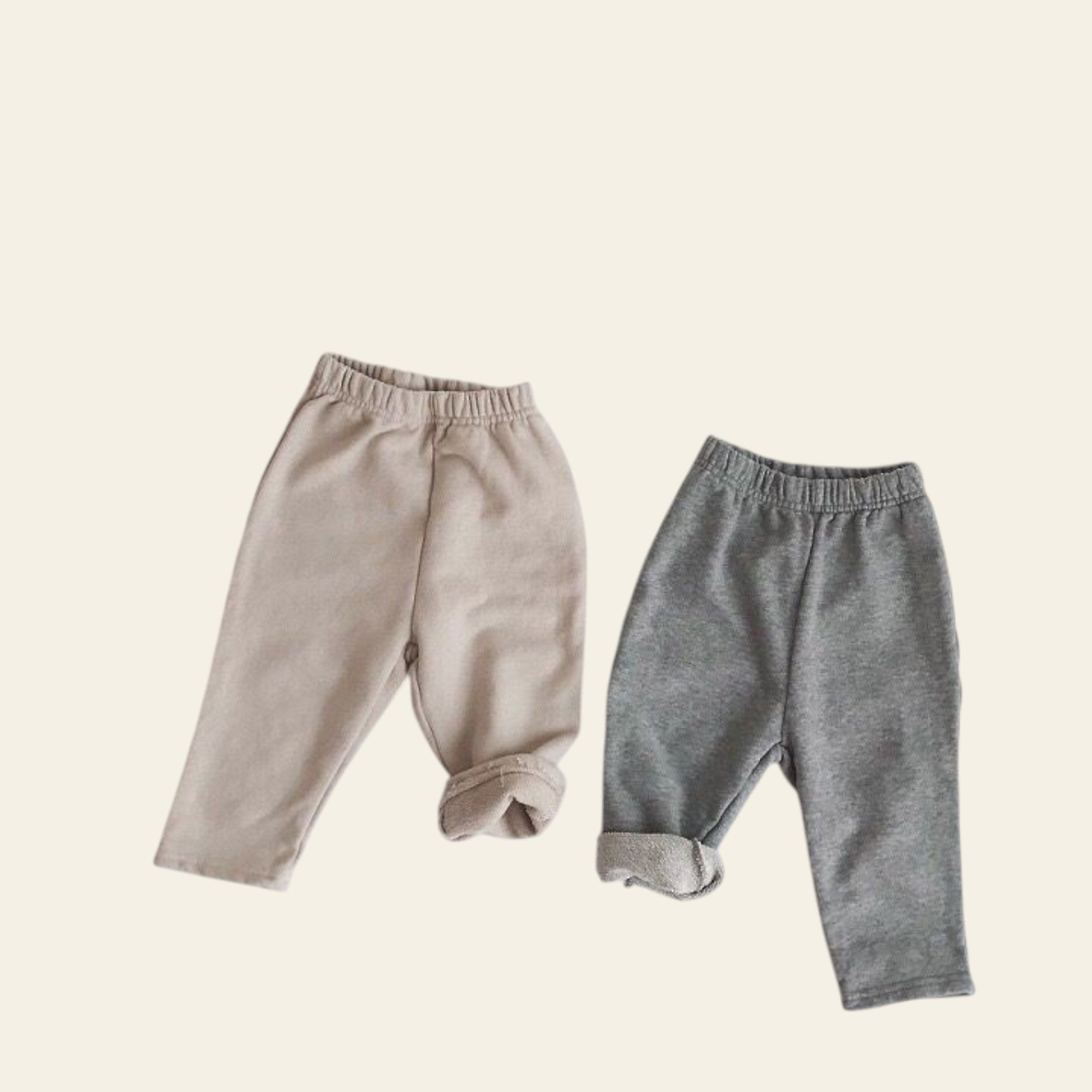 Two pairs of baby pants, one beige and one gray, on a light gray background.