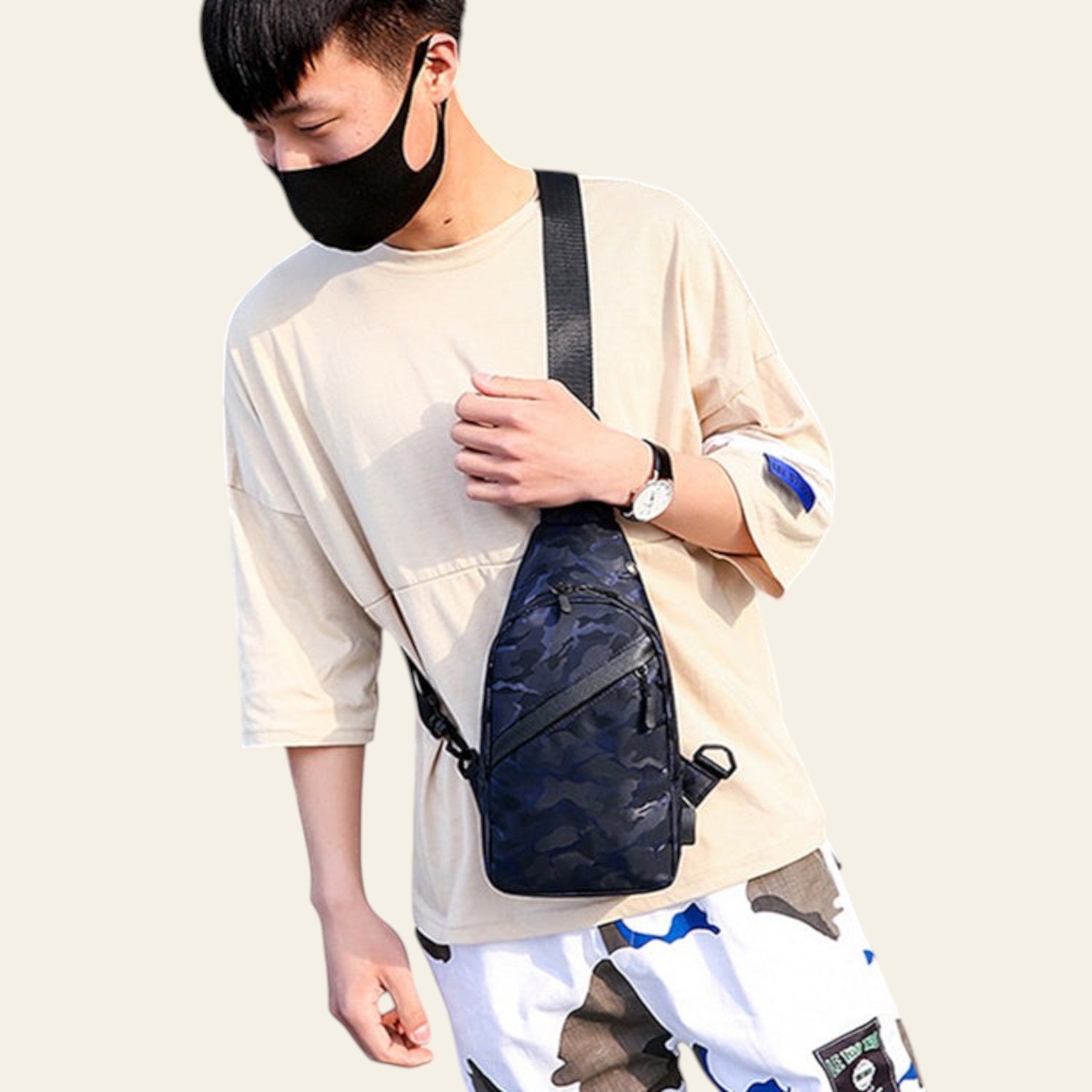 Person wearing a beige shirt and white pants with a black camouflage sling bag outdoors.