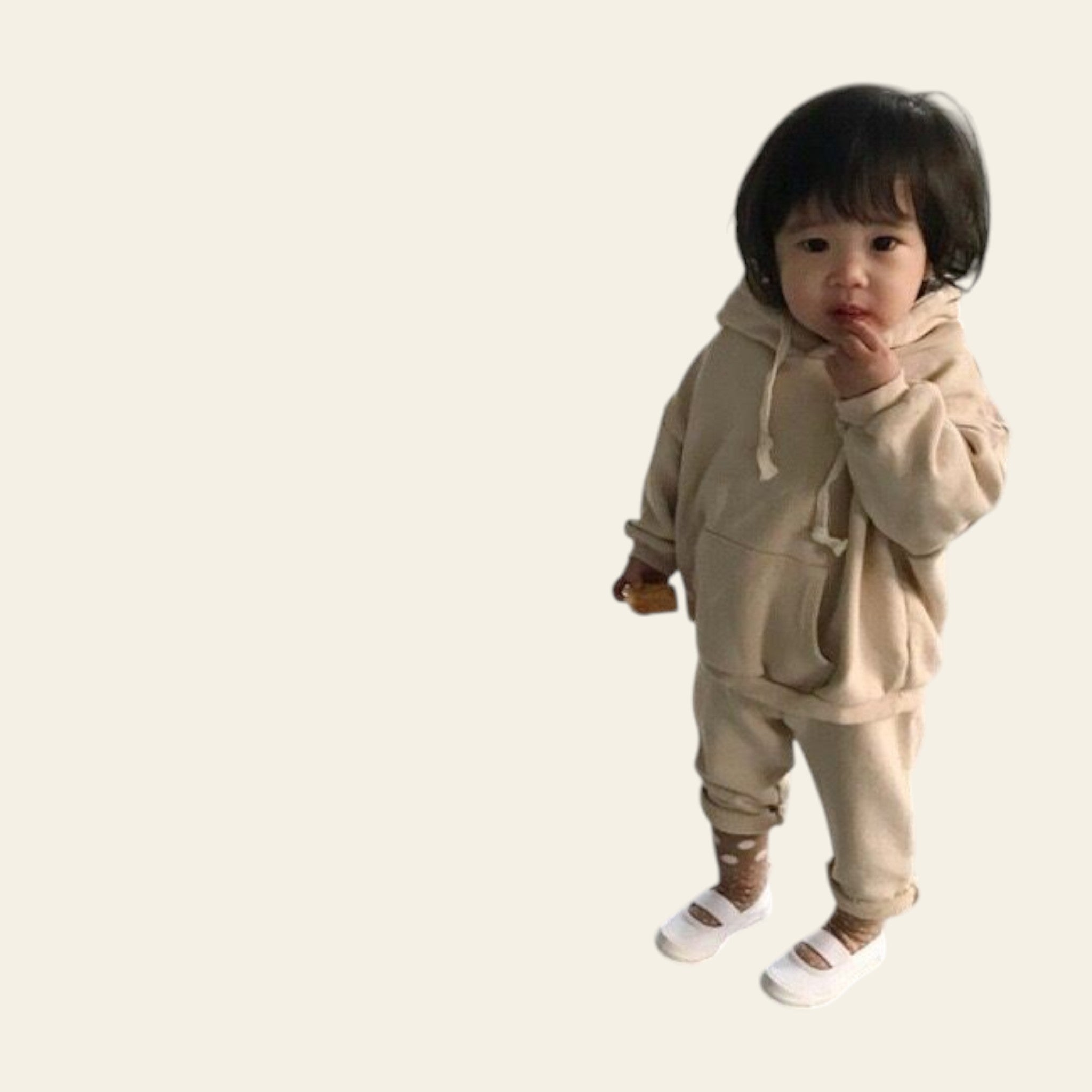 Child wearing a beige hoodie and pants standing on a concrete floor.