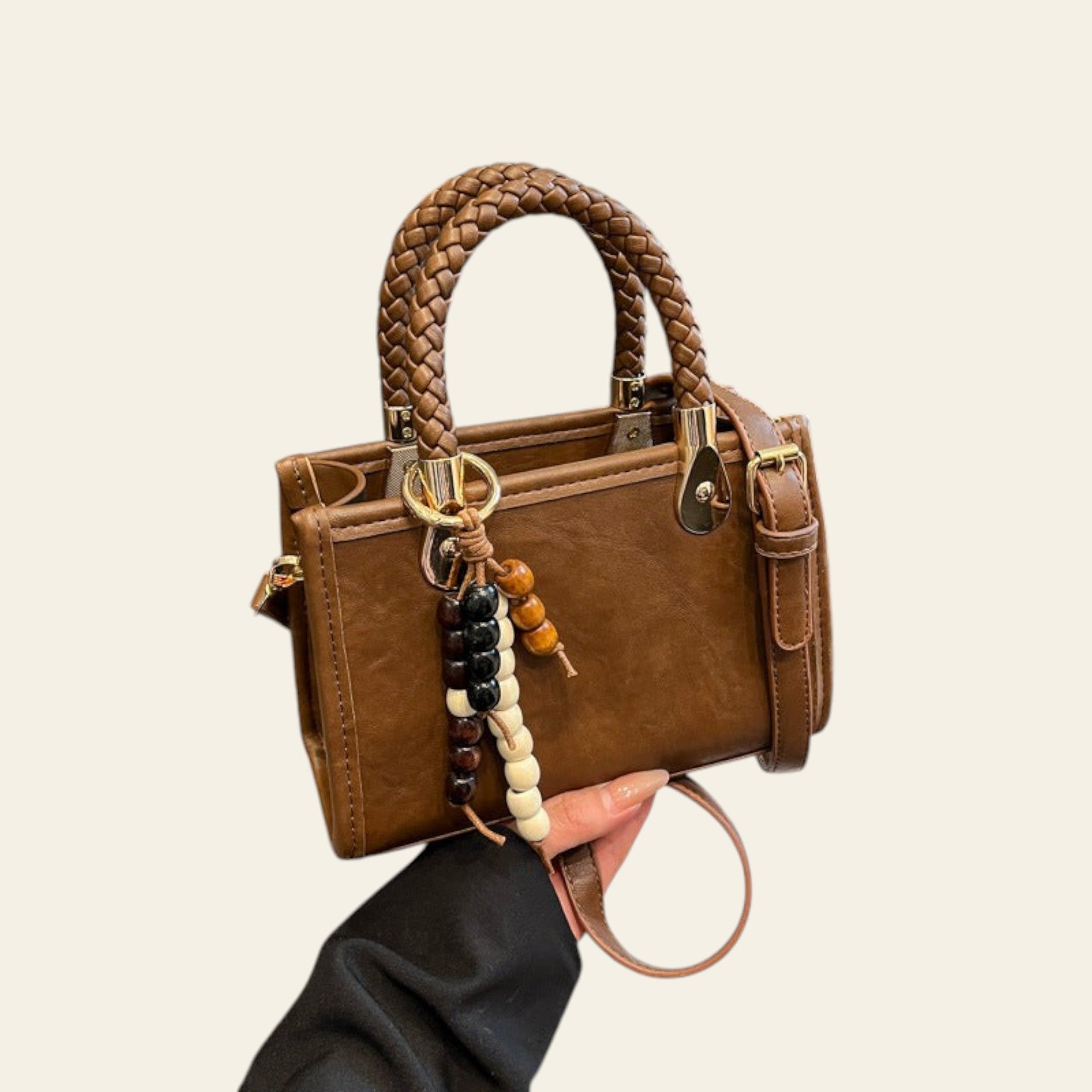 Brown handbag with braided handle held by a person wearing a black jacket.
