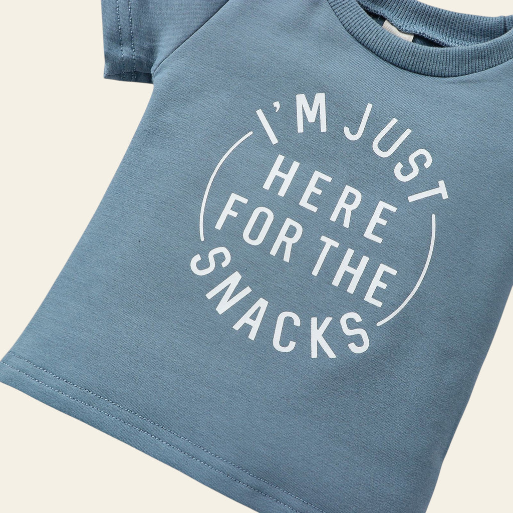 Blue t-shirt with 'I'm just here for the snacks' text on a wooden surface