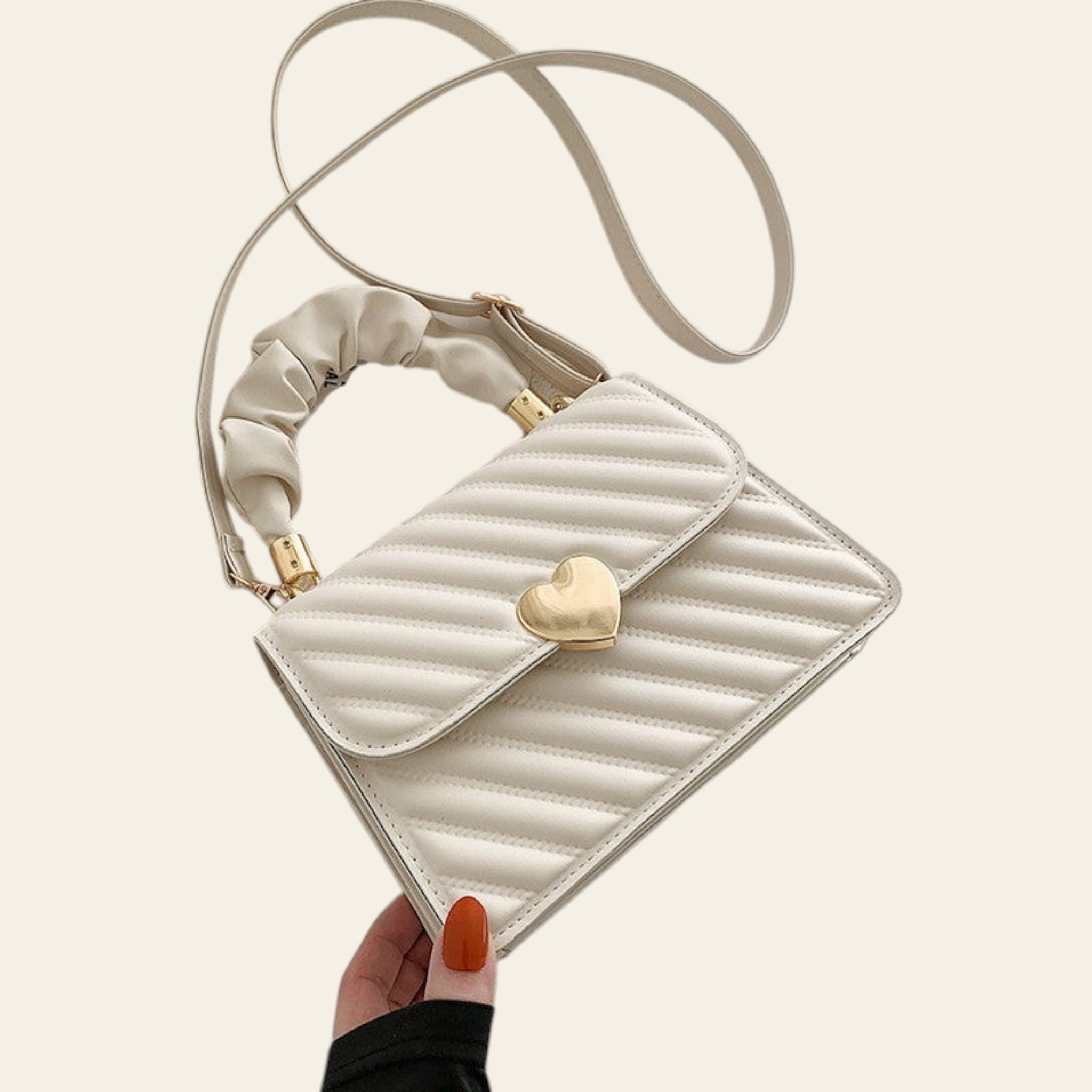 White quilted handbag with a gold heart detail held by a hand on a light background