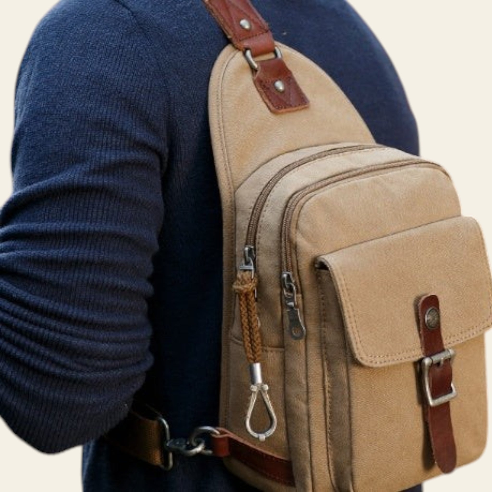 Beige sling bag with brown straps worn by a person in a blue sweater.
