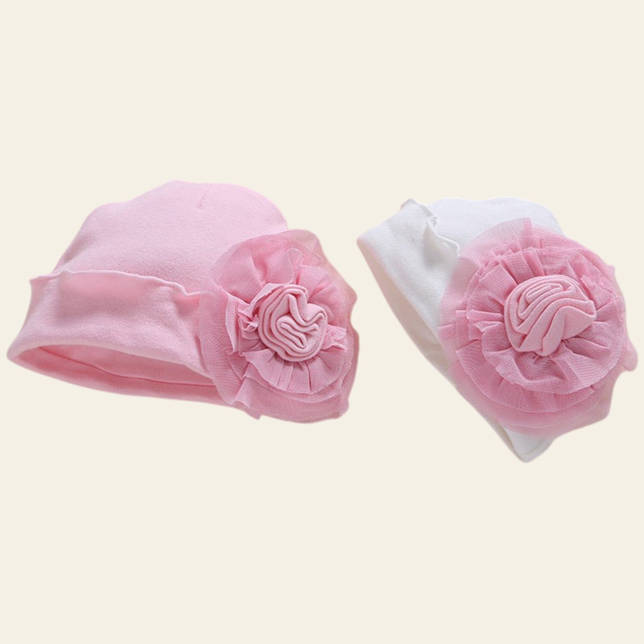 Two baby hats with pink flower embellishments on a beige background