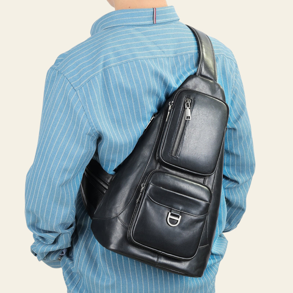 Person wearing a black leather sling bag on a plain background