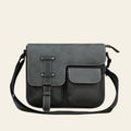 Black leather satchel bag on a wooden surface with a gray textured wall background