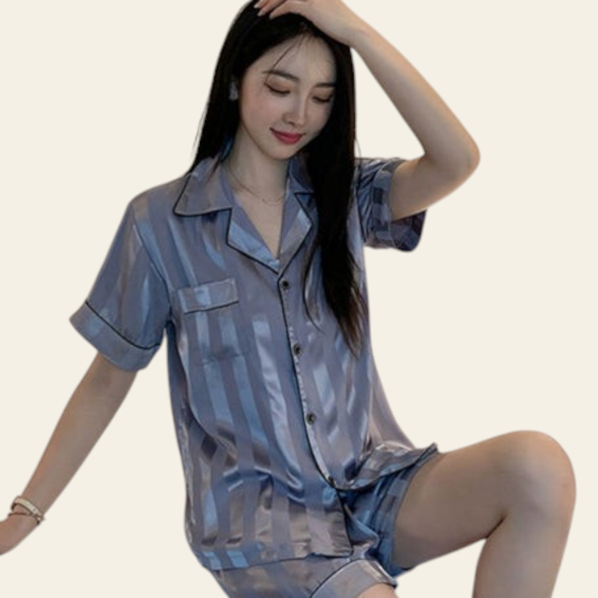 Woman wearing a blue satin pajama set sitting on a bed.