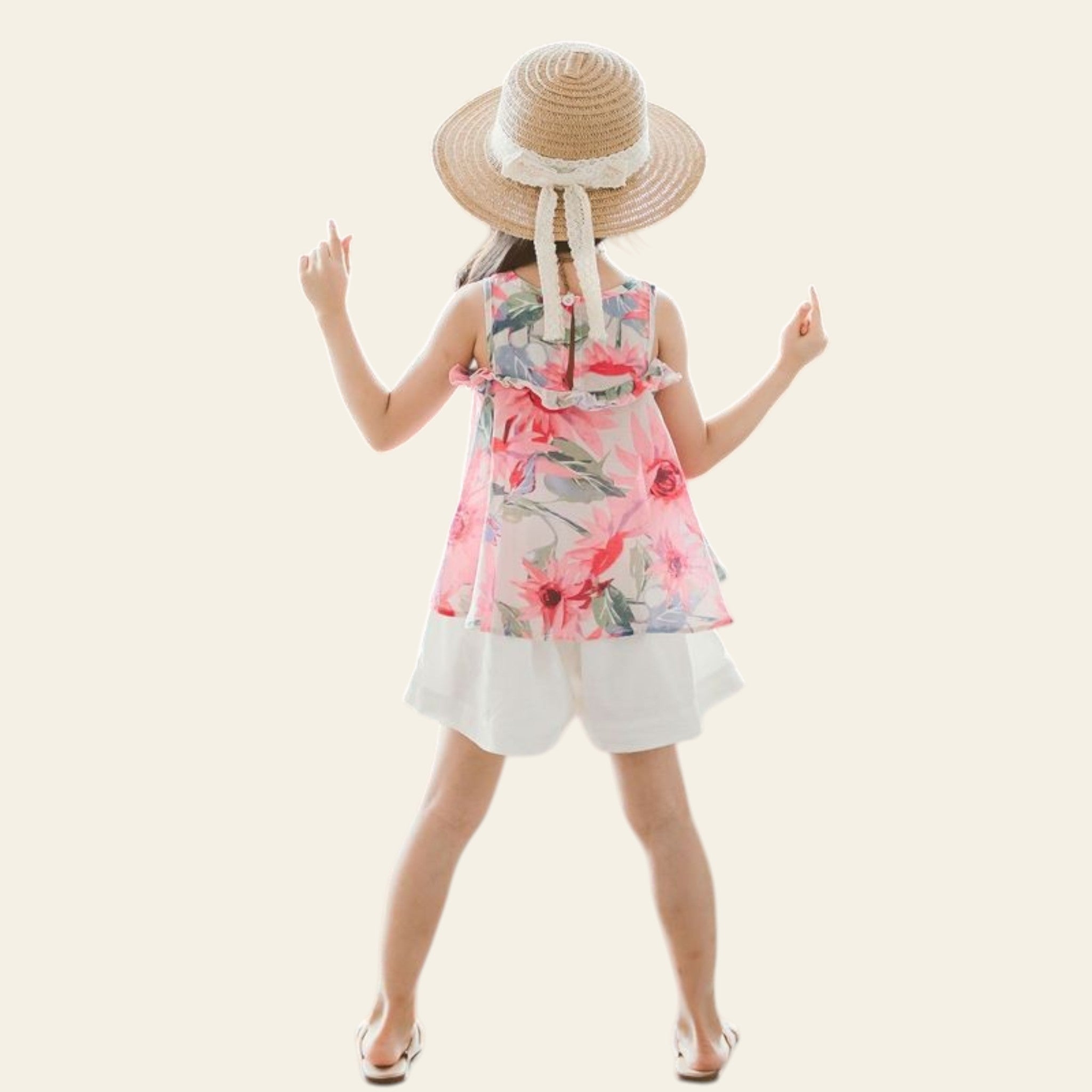 Child in a floral dress and straw hat standing on a textured surface with a plant in the background