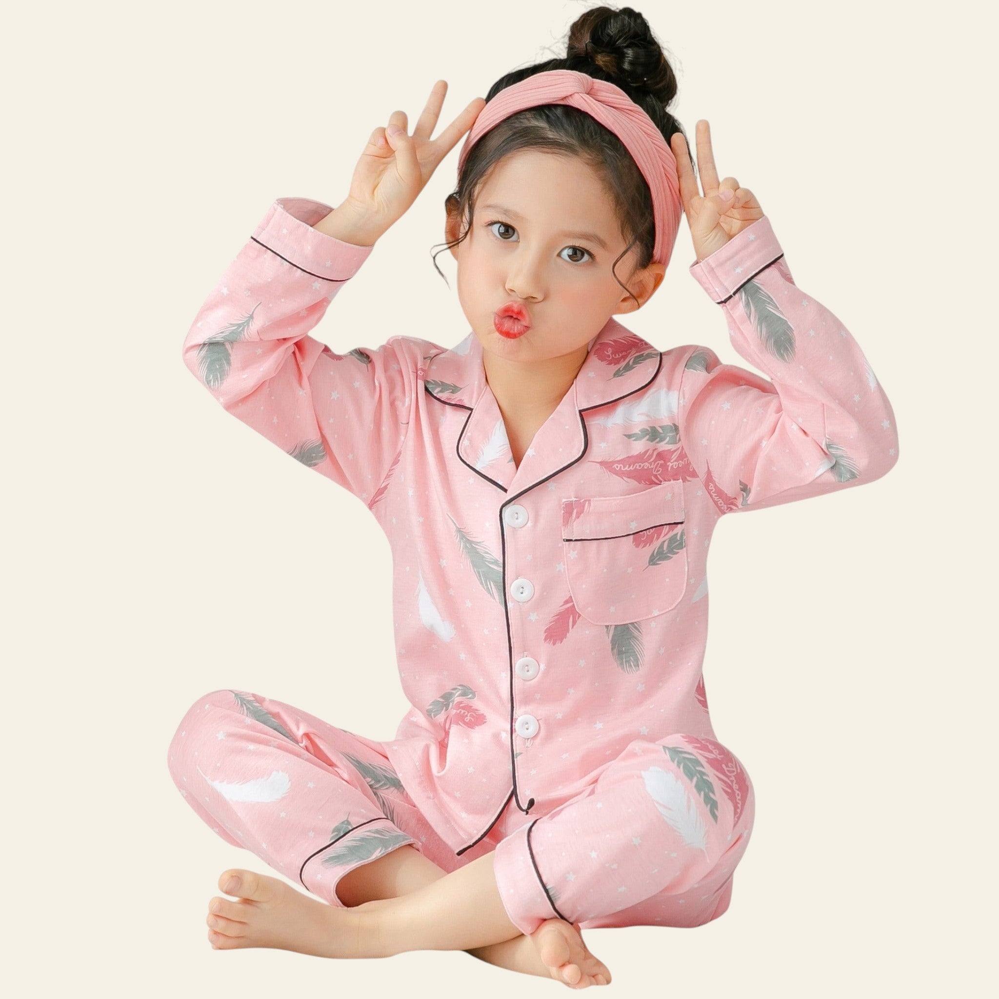 Child wearing pink pajamas with floral patterns, sitting on a bed.