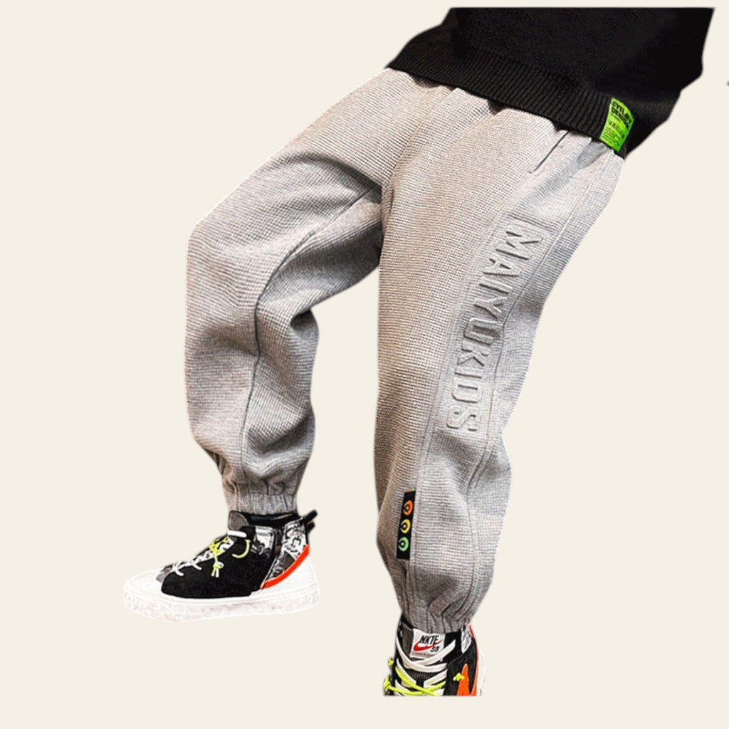 Child wearing gray sweatpants with a brand logo, standing on a wooden floor.