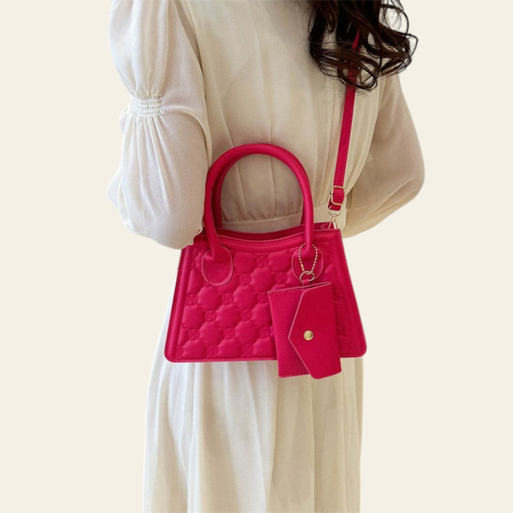 Person holding a pink quilted handbag with a matching wallet against a neutral background