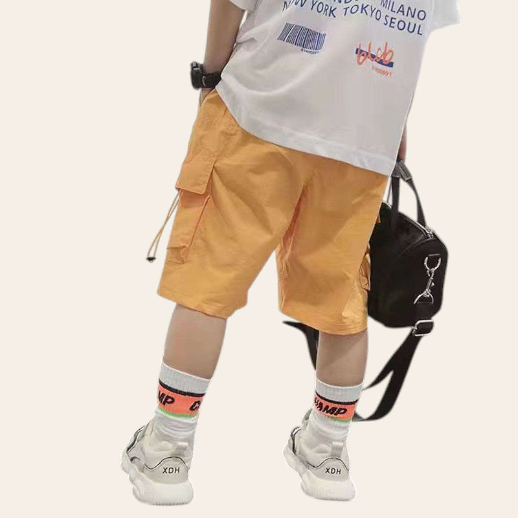 Person wearing a white t-shirt, yellow cargo shorts, and white sneakers with colorful socks on a plain background.