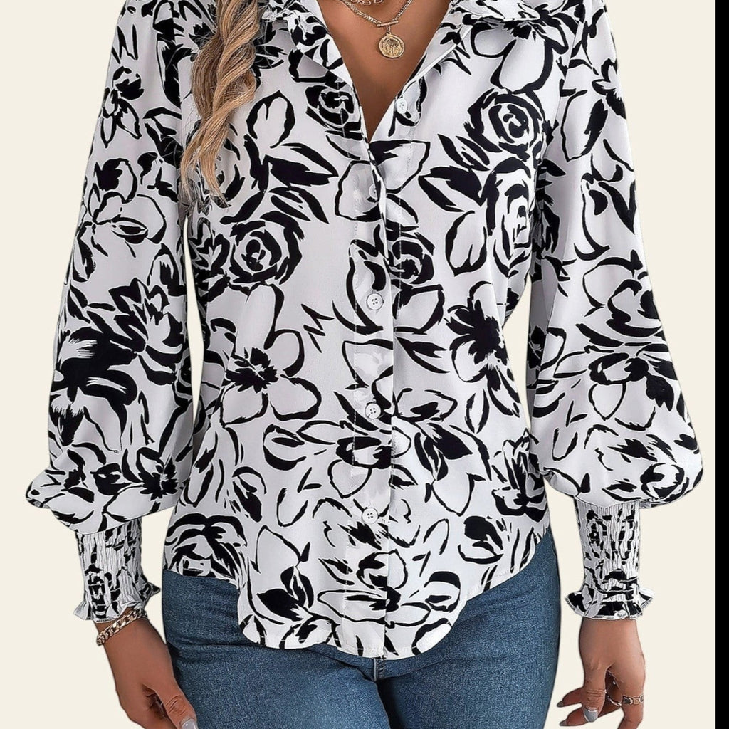 Woman wearing a black and white floral blouse with blue jeans indoors.
