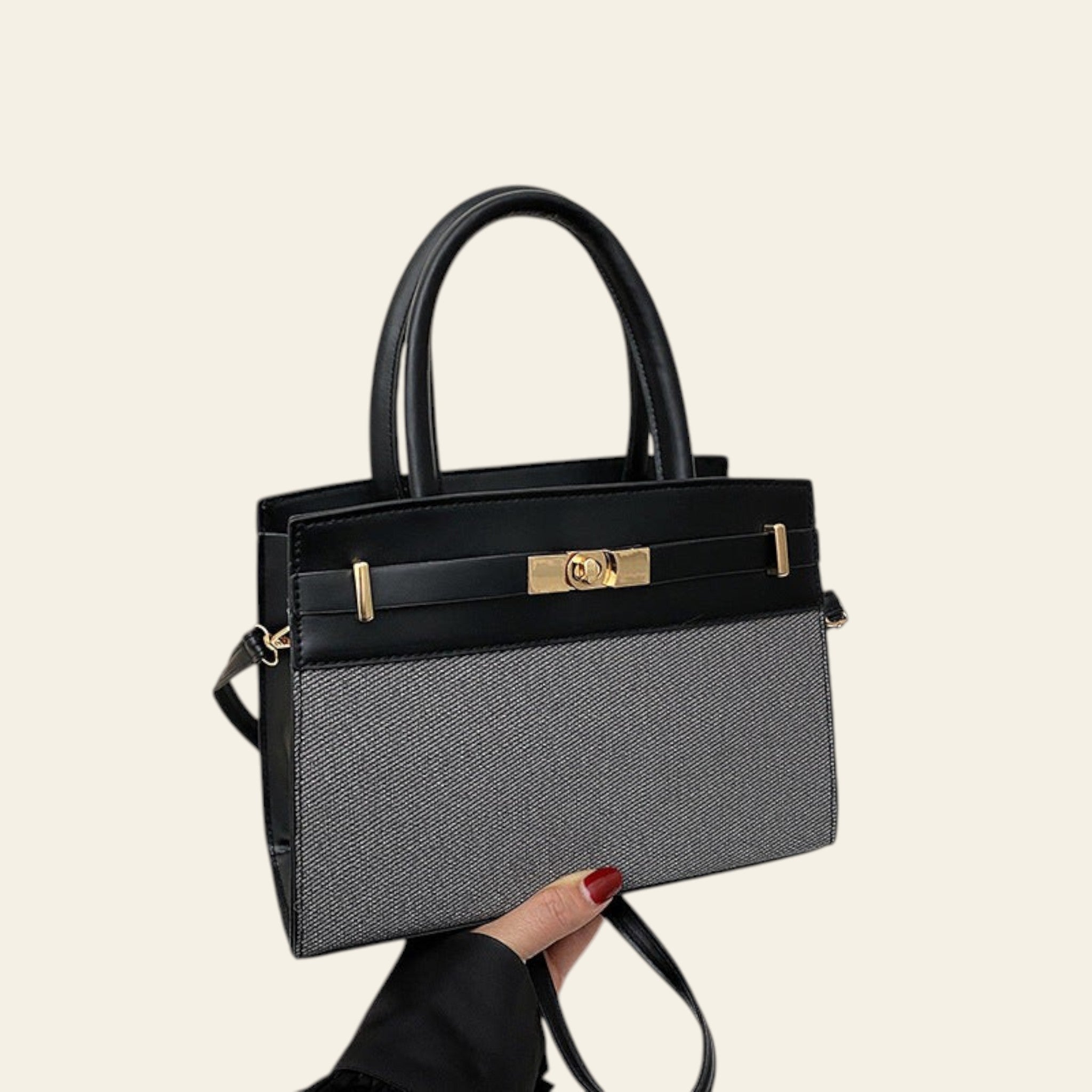 Black handbag with gold accents held by a hand on a white surface.