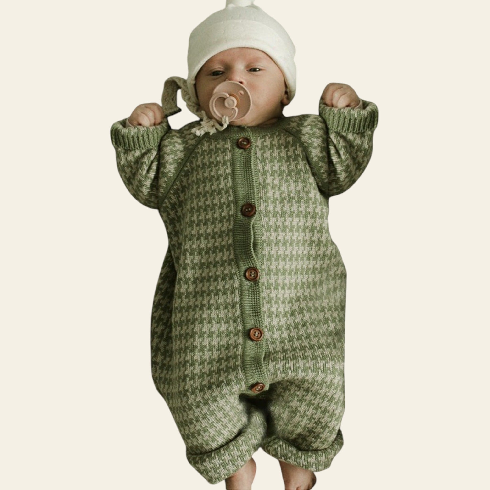 Baby wearing a green knitted outfit with brown buttons on a textured blanket.