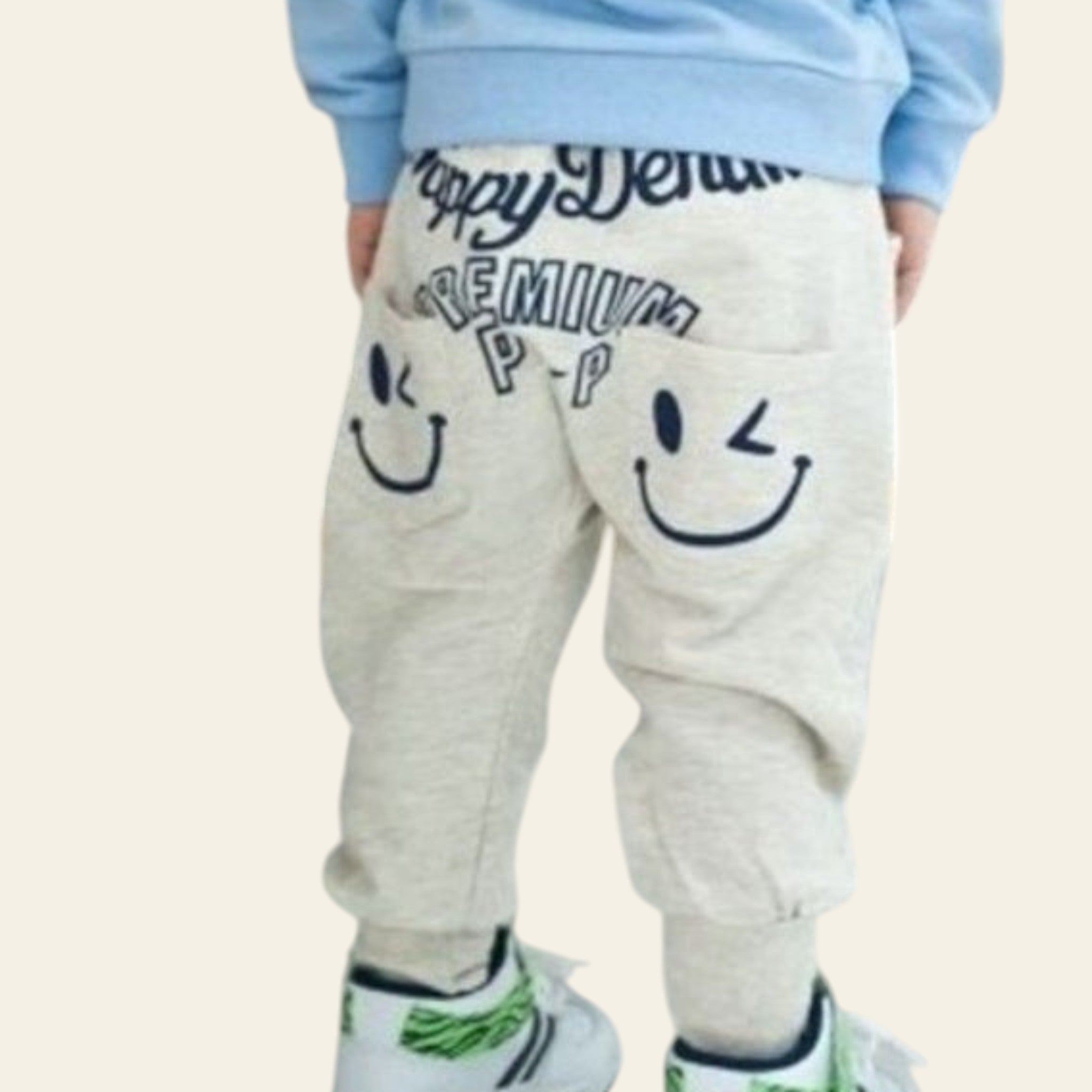Child wearing light blue hoodie and beige pants with smiley face designs, standing indoors.