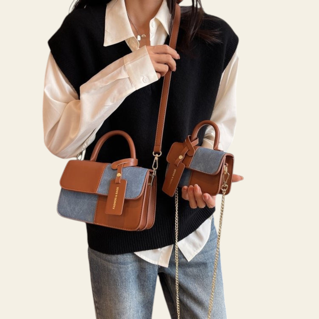 Person holding two handbags, one with a denim and brown design and the other with a chain strap, in an indoor setting.