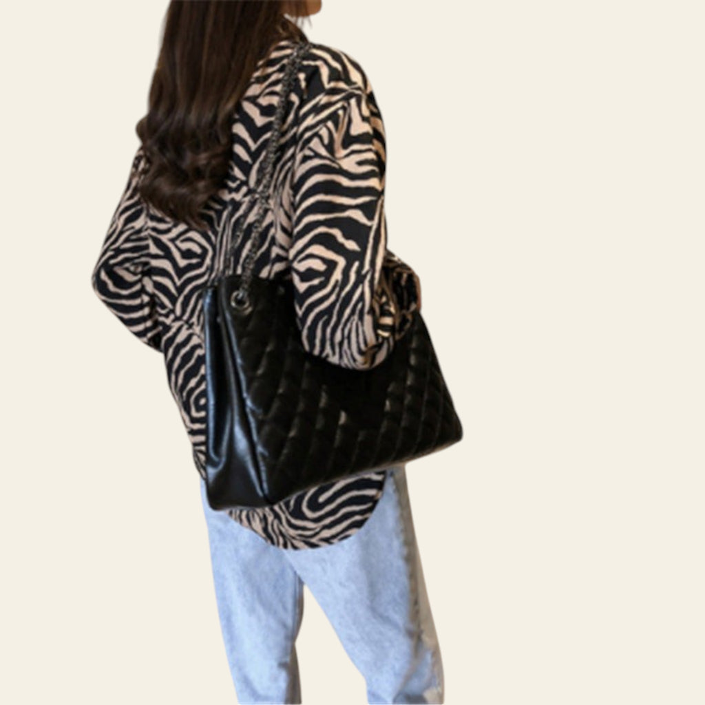 Person wearing a zebra print jacket and holding a black handbag in a kitchen.