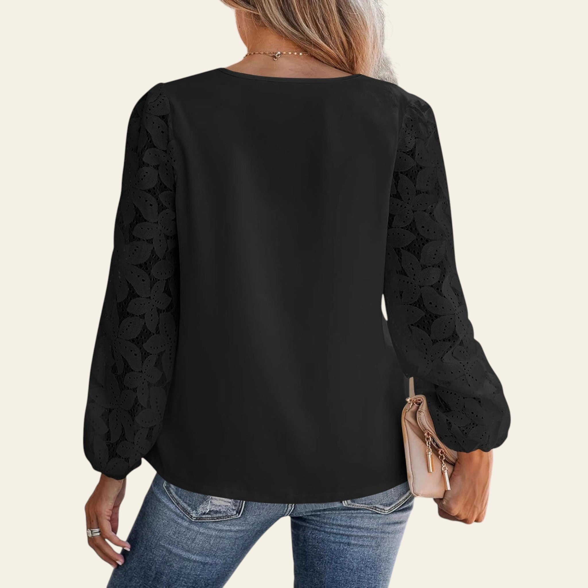 Person wearing a black blouse with lace sleeves and blue jeans, holding a beige clutch.