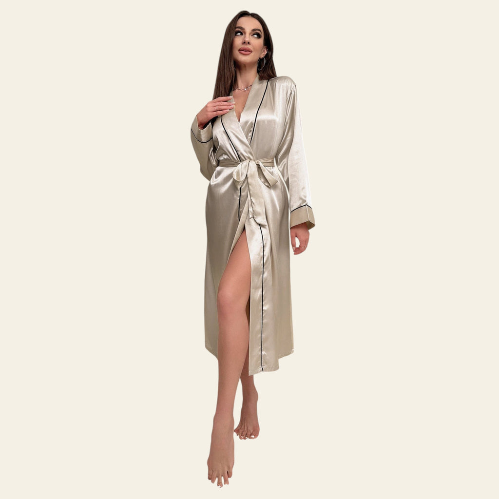 Woman in a satin robe standing in a stylish room with large windows and decorative pillows.