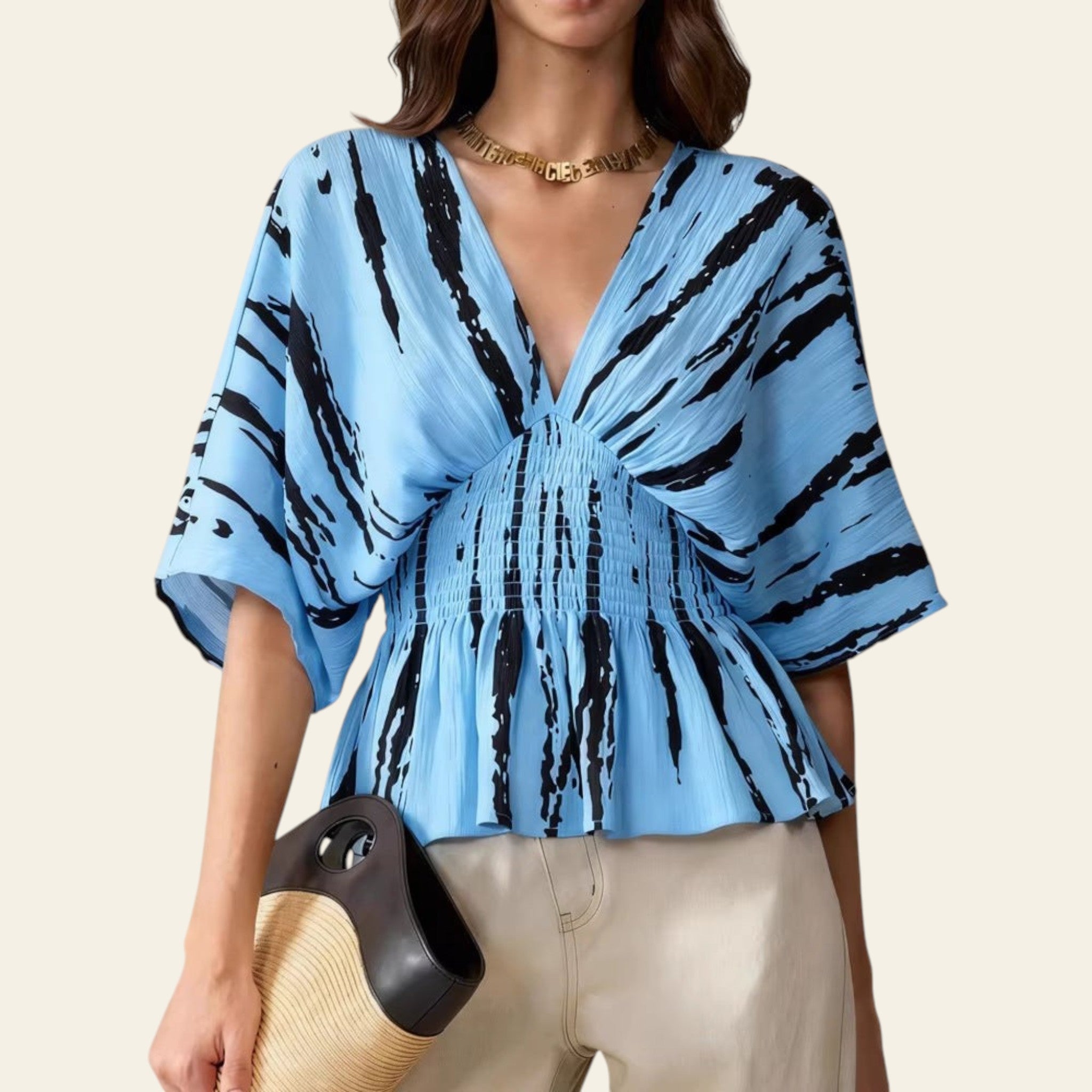 Woman wearing a blue and black patterned blouse with beige pants against a neutral background
