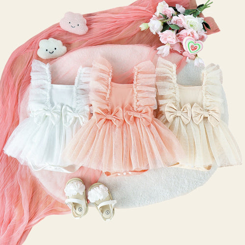 Three baby dresses in white, pink, and beige with matching shoes on a wooden surface.