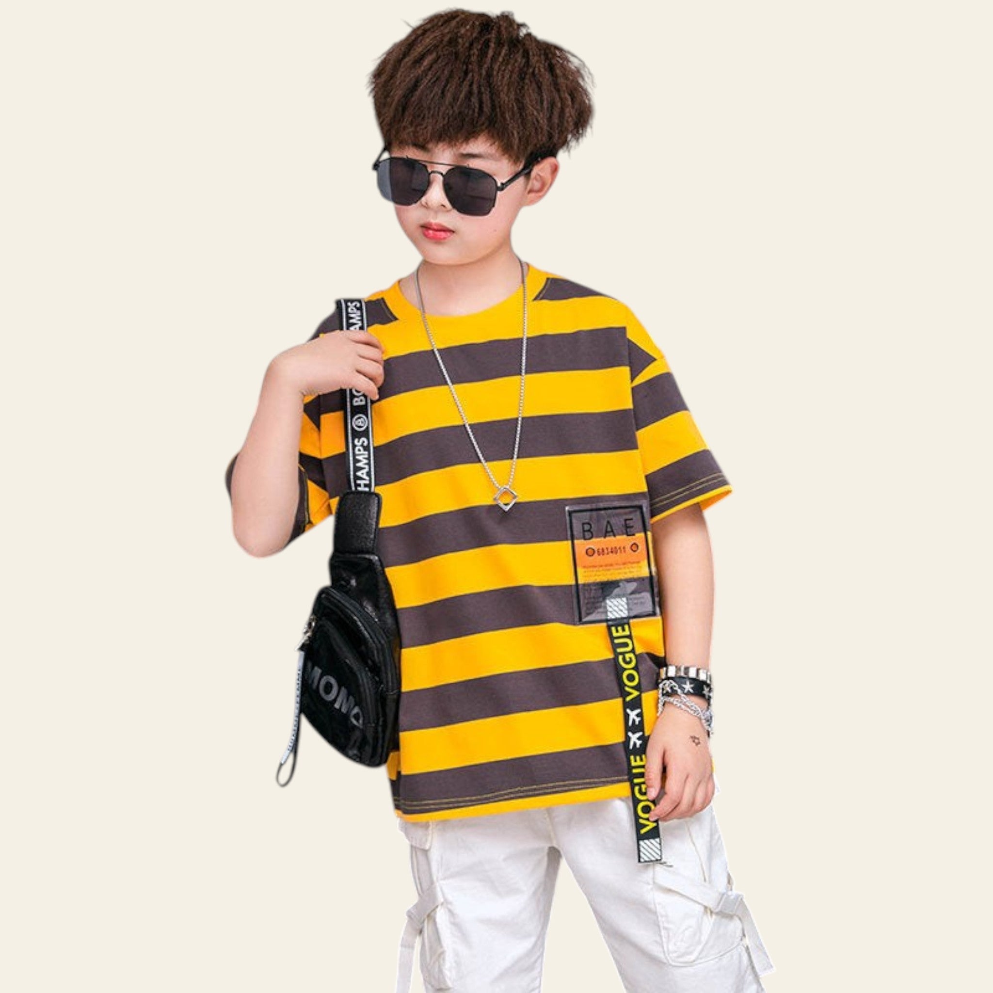 Child wearing a yellow and brown striped shirt with a black bag, standing in front of a branded backdrop.