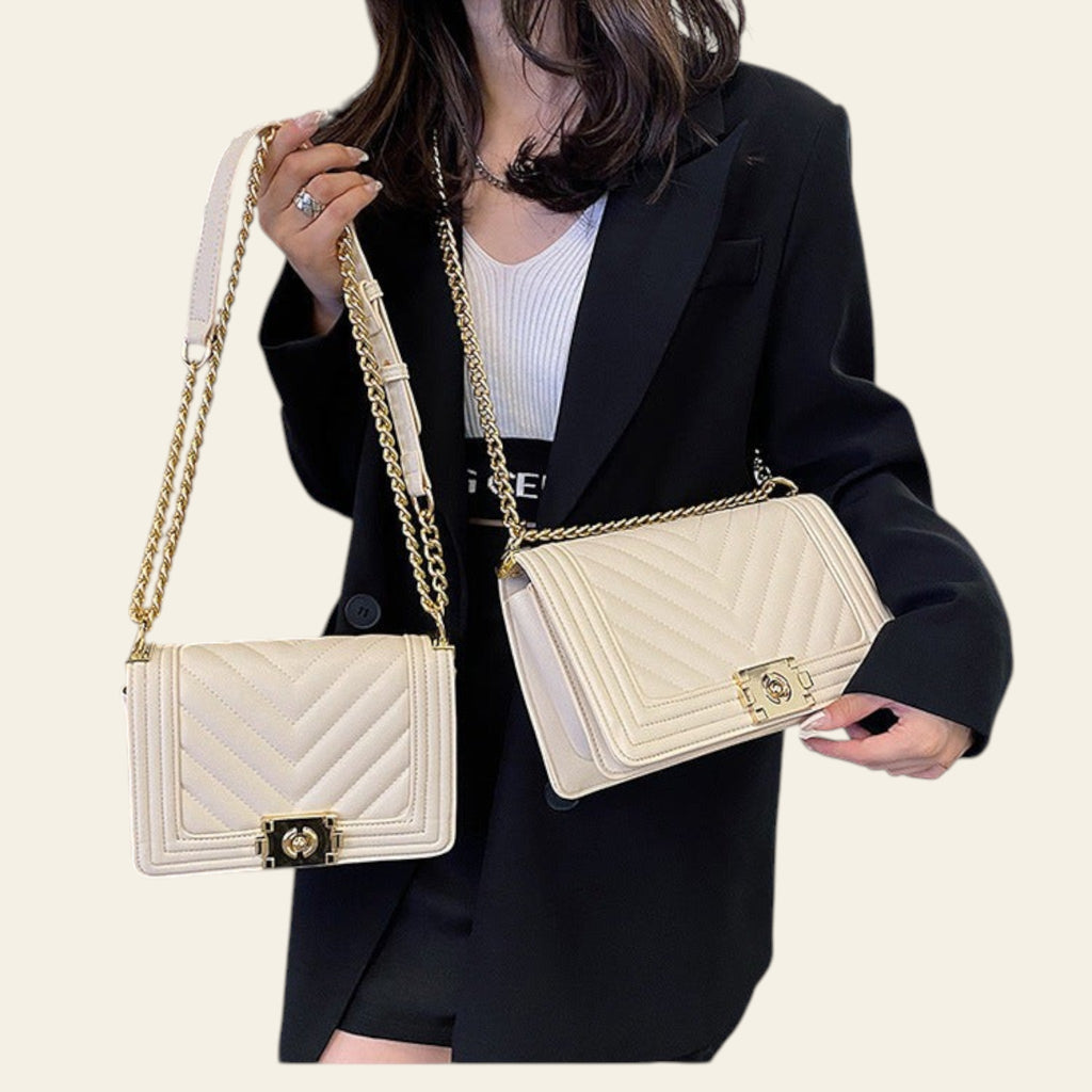 Person holding two white handbags with gold chains in an indoor setting