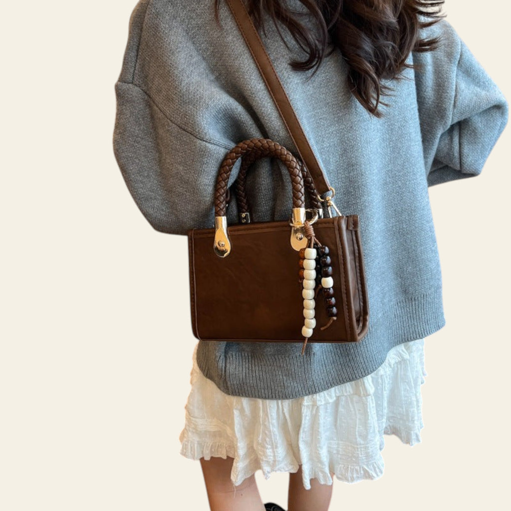 Person wearing a brown handbag with decorative elements in an indoor setting.