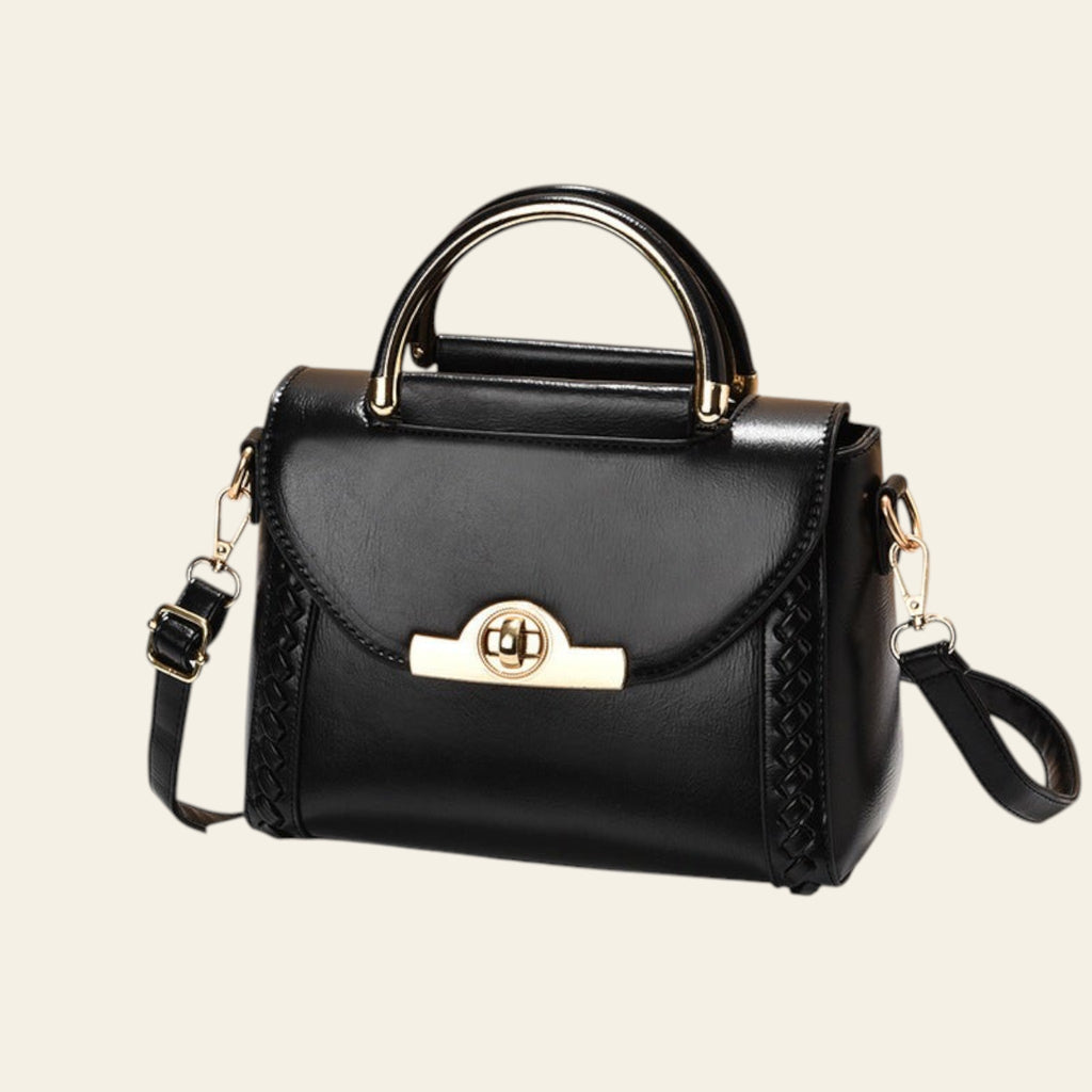 Black handbag with gold accents on a white surface and beige background
