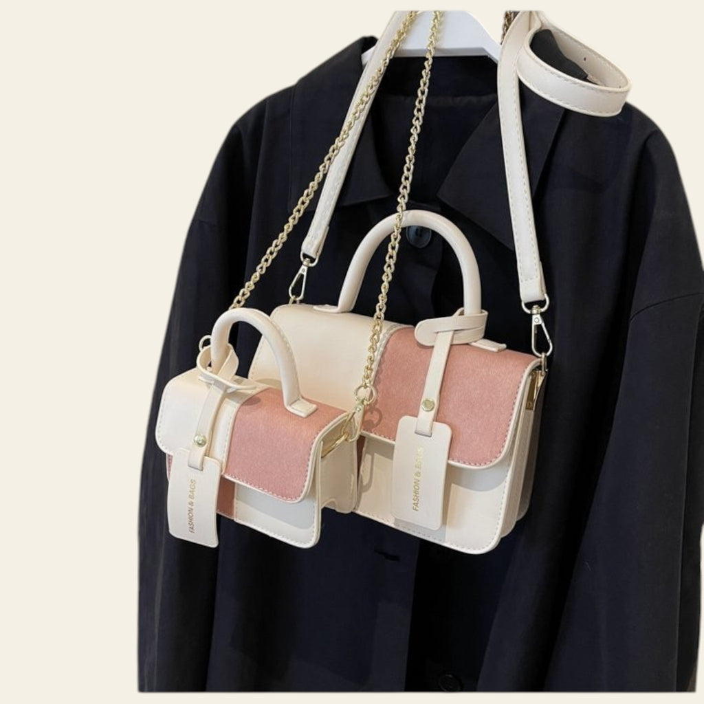 Two handbags, one pink and one white, hanging on a black garment against a beige wall.