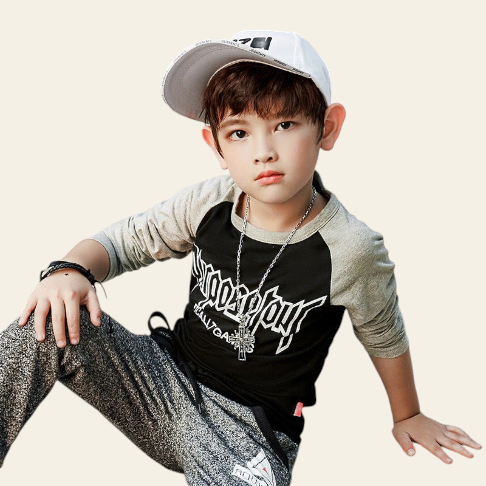 Child wearing a black and gray outfit with a cap, sitting on a concrete surface.