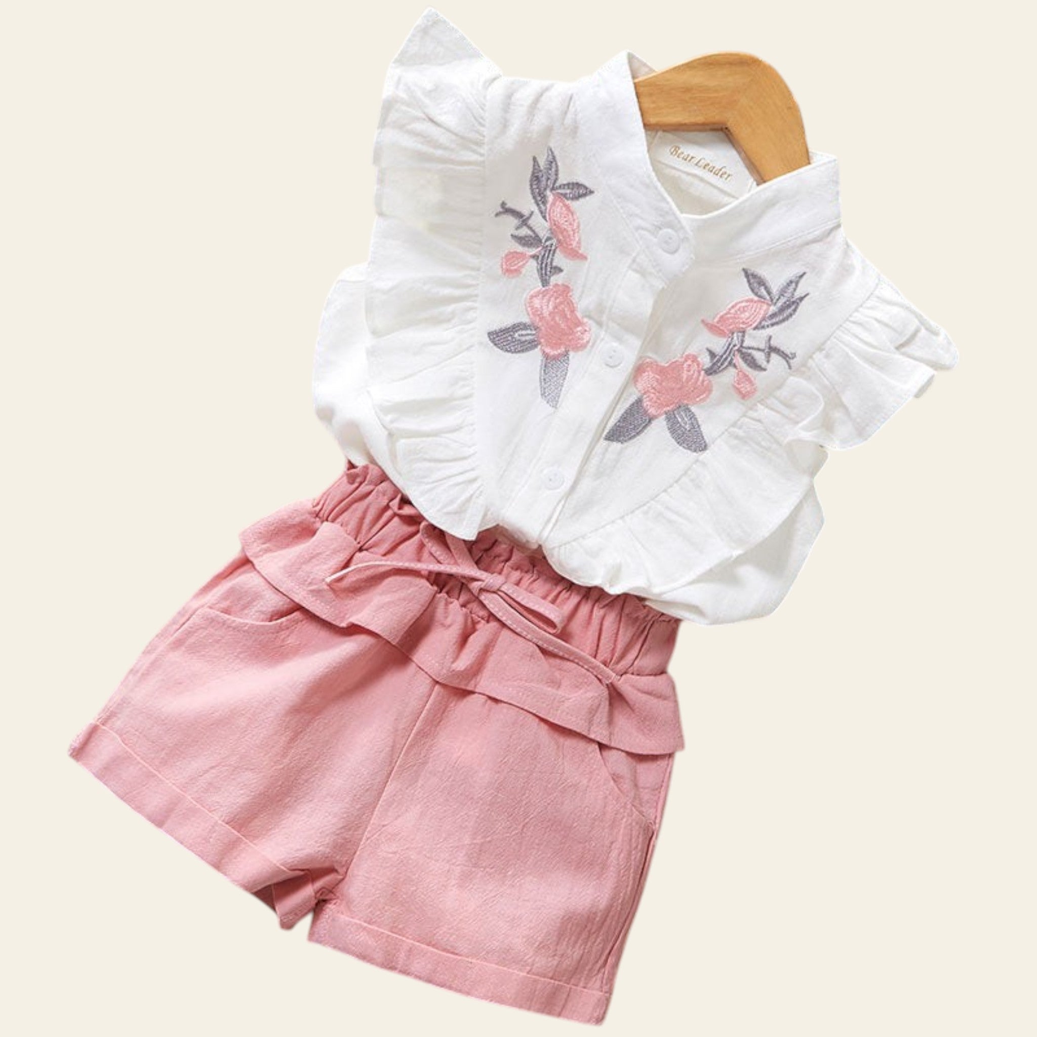 White blouse with floral embroidery and pink shorts on a wooden surface.